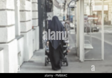 Blurred unrecognizable muslim woman wearing Veil and pushing baby stroller in European city Stock Photo