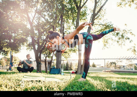White Caucasian middle age woman doing yoga in park outside on sunset. Female person stretching, performing workout outdoors. Healthy lifestyle modern Stock Photo