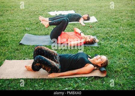 Yoga session in park on summer day. White young Caucasian woman checking her phone and surfing Internet during sport class. Modern gadgets interfering Stock Photo