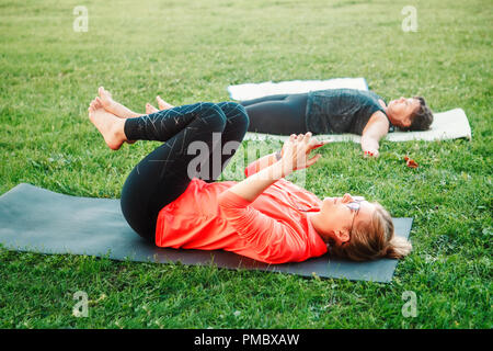 Yoga session in park on summer day. White young Caucasian woman checking her phone and surfing Internet during sport class. Modern gadgets interfering Stock Photo