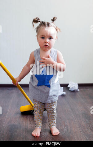 A 1.5 year old girl is engaged in household chores, sweeping the floor. Household routine, dangers for children in the house. Stock Photo