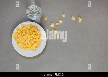 cornflakes in a white cup and a glass with water on a gray background, aesthetics of chaos Stock Photo