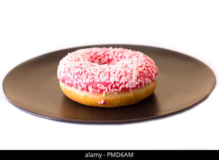 Brightly pink donut on black ceramic plate on white background. Stock Photo