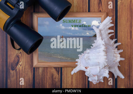 closeup of big black binoculars, a beautiful sea shell and frame with an inscription on a wooden background Stock Photo