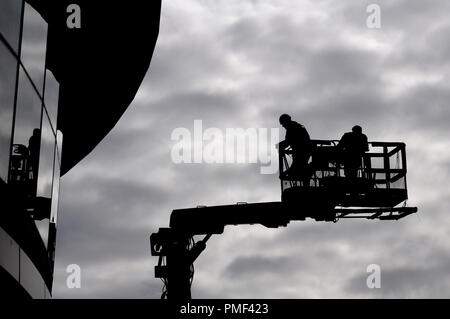 Two construction workers in silhouette against grey sky on a hydraulic lifting ramp Stock Photo