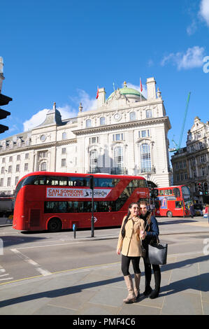 Two smartly dressed teenage girls taking a picture with a selfie stick at Piccadilly Circus looking towards Hotel Cafe Royal on Regent Street, London. Stock Photo