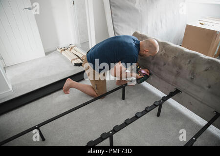 Mature man is using a power drill to put together a bed in his new home. Stock Photo