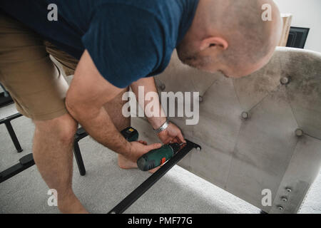 Mature man is using a power drill to put together a bed in his new home. Stock Photo