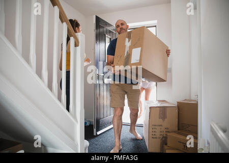 Mature man is carrying boxes in to his new home. His daughter and wife can be seen behind him. Stock Photo