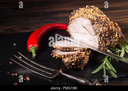 Piece and slices of roasted meat. Cold-boiled baked pork with mustard grains on dark background. Stock Photo