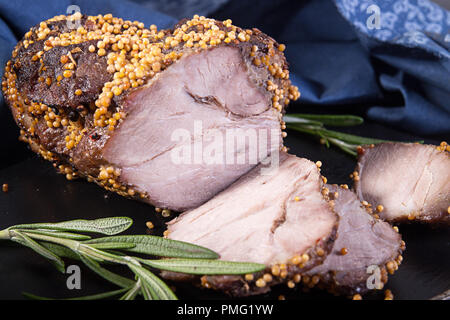 Piece and slices of roasted meat. Cold-boiled baked pork with mustard grains on dark background. Stock Photo