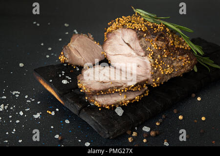 Piece and slices of roasted meat. Cold-boiled baked pork with mustard grains on dark background. Stock Photo