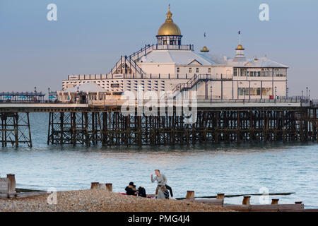 People on Eastbourne beach with the pier behind them, in the county of East Sussex on the south coast of England in the UK. Stock Photo