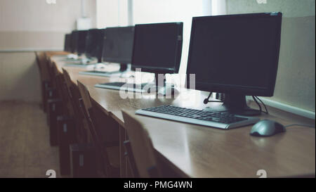 Computer monitors, mouses and keyboards on the tables. Education room in school. Studying at school. Modern computers. Study stuff. Many monitors room. Stock Photo