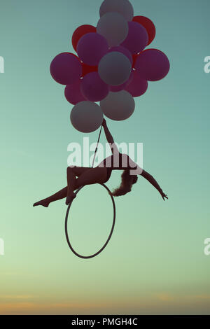 Girl hovers in the air on balloons sitting on an acrobatic ring. Stock Photo