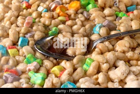 Close view of a spoon in generic crunchy breakfast cereal with fruit flavored bits plus milk and maple syrup. Stock Photo