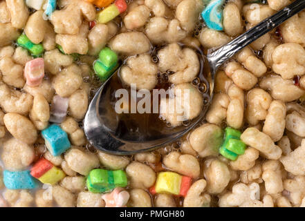 Top close view of a spoon in generic crunchy breakfast cereal with fruit flavored bits plus milk and maple syrup. Stock Photo