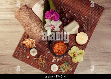 Spa and wellness setting with orchid flowers, bowl with sea salt, seashell, bottle with aromatic oil, soap, candles and towels on bamboo napkin Stock Photo
