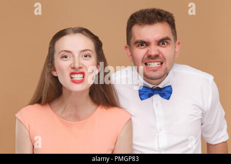 closeup portrait of handsome man and beautiful woman or young couple looking at camera with funny face and showing their clenching teeth. indoor studi Stock Photo