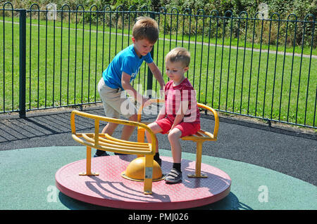 Two small boys playing on a roundabout in a play park. Stock Photo