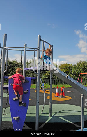Four year old boy and seven year old boy playing on a slide in a play park. Stock Photo