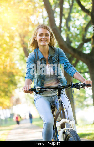 Young woman ride bike in autumn park. Enjoying while cycling in nature during autumn day. Stock Photo