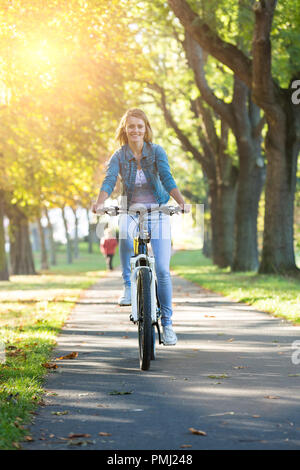 Young woman ride bike in autumn park. Enjoying while cycling in nature during autumn day. Stock Photo