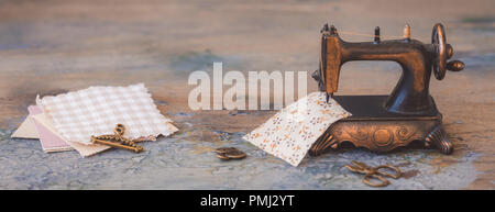 Vintage mini sewing machine with scissors, buttons and fabric on rustic background, toned Stock Photo