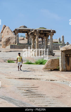 Lone man walking beside huge boulders and stone structures on the Hemakuta Hill at Hampi, Karnataka, India Stock Photo