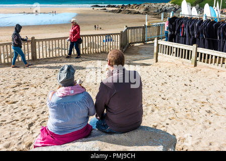 Holidaymakers on a staycation holiday enjoying an ice cream as they sit gazing out over Fistral Beach in Newquay in Cornwall. Stock Photo