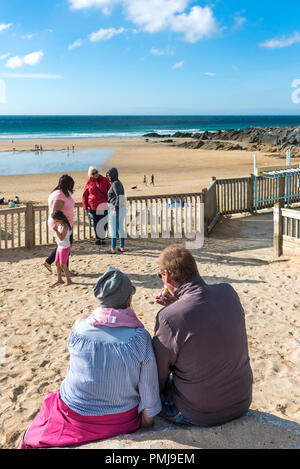 Holidaymakers on a staycation holiday enjoying an ice cream as they sit gazing out over Fistral Beach in Newquay in Cornwall. Stock Photo