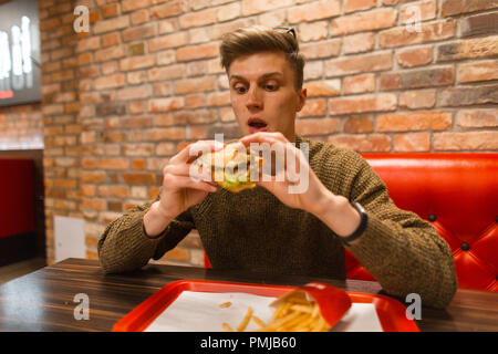 Concept of fast food. Man hipster eating a hamburger and french fries in a restaurant Stock Photo