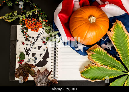halloween.an orange pumpkin with an American flag, a writing pad with a black Jack painted on it. the dry leaves empty space. Stock Photo
