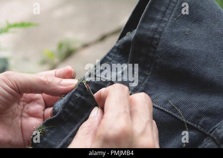 Hand holding and using sewing seam ripper. Ripping a seam with a ripper. Stock Photo