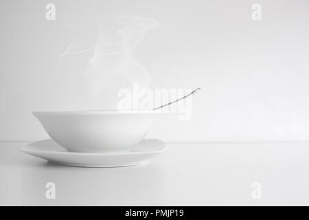 Hot soup with steam based on a broth and bouillon receipt served on a clay white round plate. Empty copy space and white background. Stock Photo