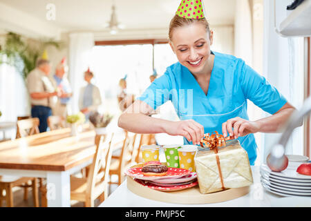 Smiling caregiver packs a present on a birthday party in the retirement home Stock Photo