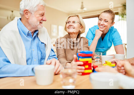 Nursing care takes care of demented senior citizens playing with building blocks Stock Photo