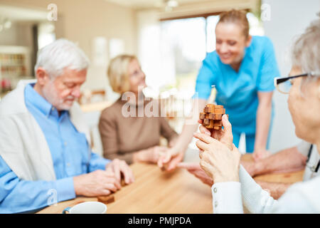 Group of seniors with dementia in retirement home playing with a wooden puzzle as a patience game Stock Photo