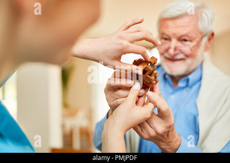 Caregiver and senior with dementia together hold a wooden puzzle in nursing home Stock Photo