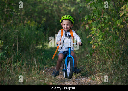 A little boy on a balance bike performs a jump on a path in the forest on a summer sunny day Stock Photo