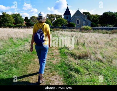 Walker on public foot path at Snow Hill going to the style in the flint wall over to st peter and paul church West Wittering, West Sussex, England, UK Stock Photo