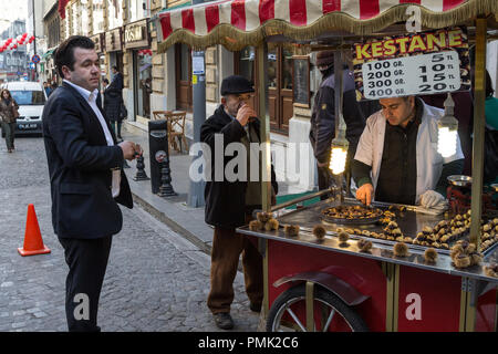 ISTANBUL, TURKEY - DECEMBER 28, 2015: Old men drinking tea and chatting next to a kiosk roasting and selling chestnuts, a typical Istanbul street food Stock Photo