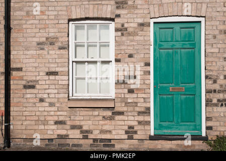 Green pastel vintage front door on a restored brick wall of a Georgian house residential building with white wooden sash window Stock Photo