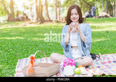 cute teen drinking hot milk while picnic sitting on mat outdoor green park holiday relax. Stock Photo