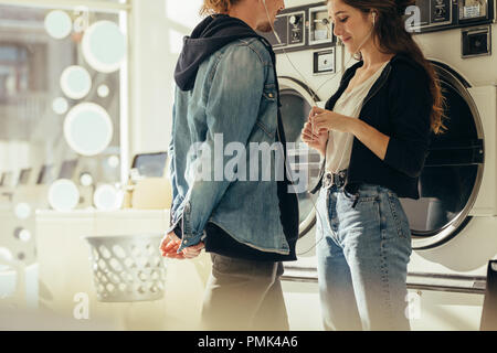 Couple sharing earphones listening to music standing in a laundry room. Couple in love standing facing each other in a laundry room. Stock Photo