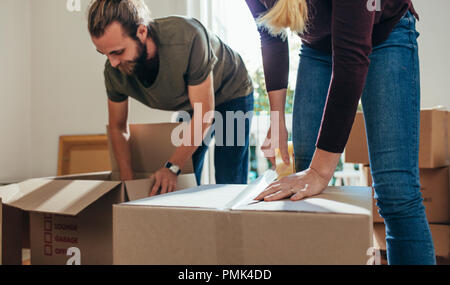 Couple packing their household articles in packing boxes. Woman putting an adhesive tape on a packing box while a man fills items in a packing box. Stock Photo