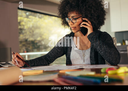 Businesswoman talking on smartphone and working in office. African female architect sitting at his workplace at home. Stock Photo
