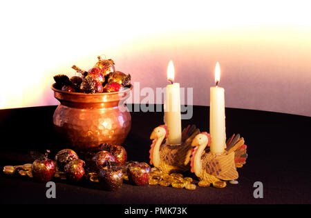Two turkey candle holders with lit candles burning next to a copper filled with red and gold apples spilling out from it set on black tablecloth. Stock Photo
