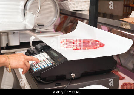 Butcher weighing meat at display cabinet in the butchery Stock Photo