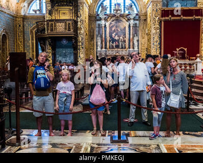 People with strange expressions on their faces listen to their audio guides, at St John's Cathedral, Valletta, Malta, Europe Stock Photo